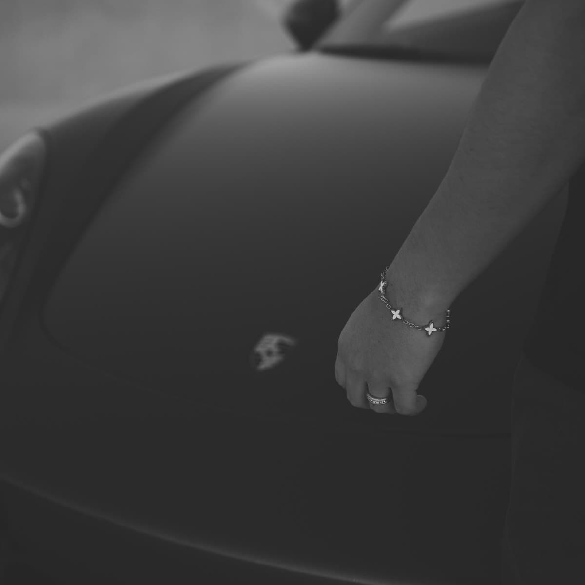 Silver charm bracelet photographed on the hood of a black Porsche
